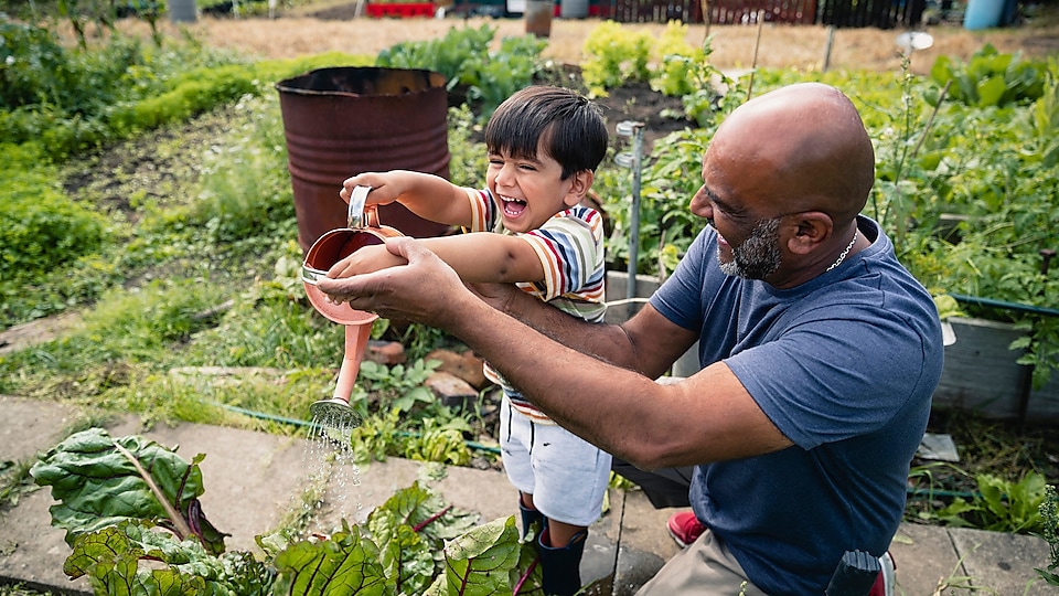 Moški pomaga nasmejanemu otroku zalivati rože na vrtu