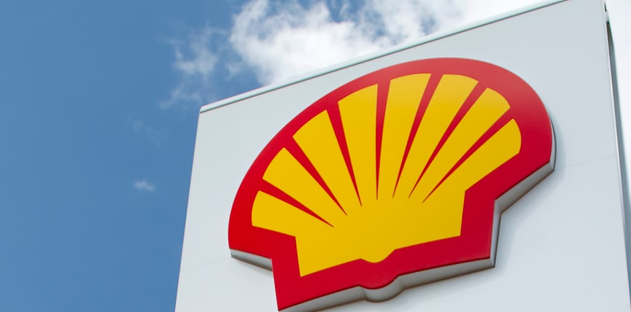 Bel Pilon na katerem se nahaja rdeče-rumen Shellov logotip in v ozadju modro nebo in bel oblak