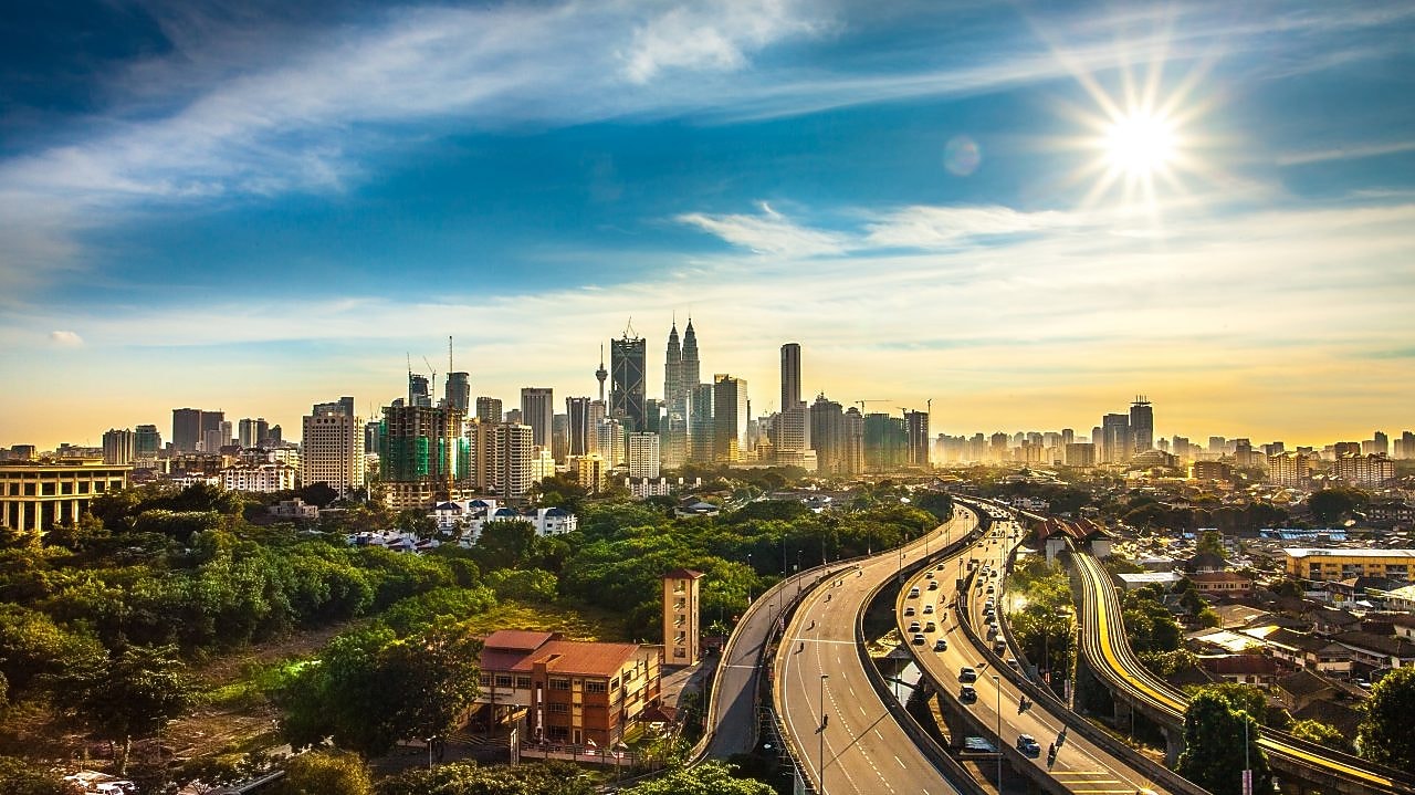 Veliko mesto z visokimi zradbami prikazano iz oddaljene perspektive, v katero pelje široka cesta.