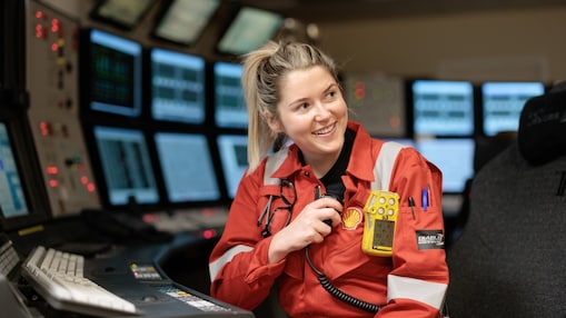 Female technician in red PPE with Shell logo on it, working in front of multiple screens