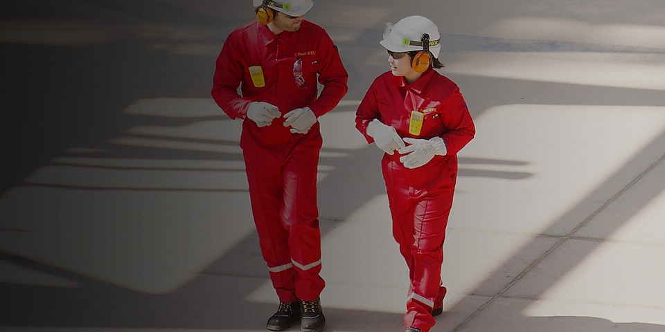 Delavec in delavka hodita, oblečena v rdeč kombinezon in z belo čelado ter zaščito na ušesih