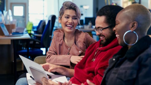 Tri osebe skupaj sedijo v pisarni, si ogledujejo papirje in se smejejo