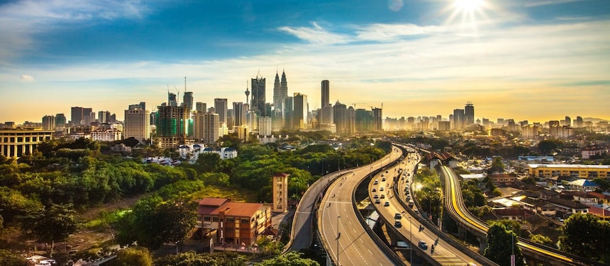 Veliko mesto z visokimi zradbami prikazano iz oddaljene perspektive, v katero pelje široka cesta.