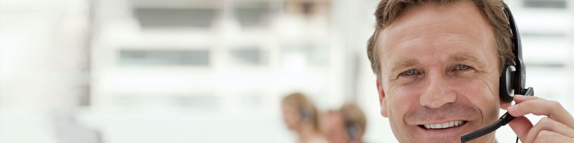 A man wearing a headset and having a phone call. Two more people in the background doing the same - blurred out.