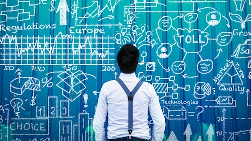 A man with yellow suspenders is looking  at a wall with different tolling-related chalk drawings.