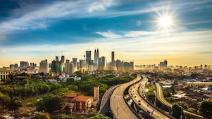 Veliko mesto z visokimi zradbami prikazano iz oddaljene perspektive, v katero pelje široka cesta.