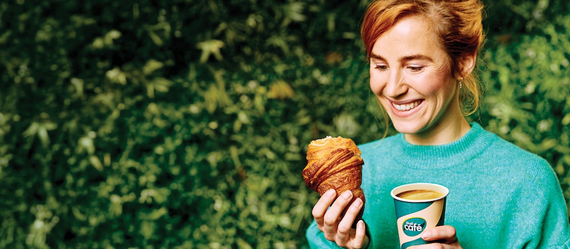 Mlada ženska z oranžnimi lasmi, ki v eni roki drži rogljiček in v drugi kavo