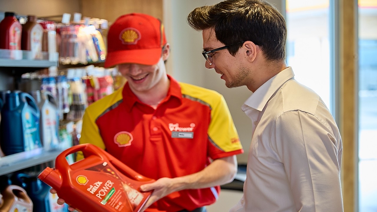 Zaposleni na Shell bencinskem servisu, ki drži rdečo motorno olje Shell Helix Power in ga predstavlja stranki.